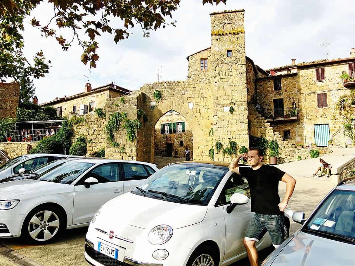 Monticchiello Italy Tuscany Town, Italy, man standing leaning on a small white FIAT car, parked cars, stone buildings