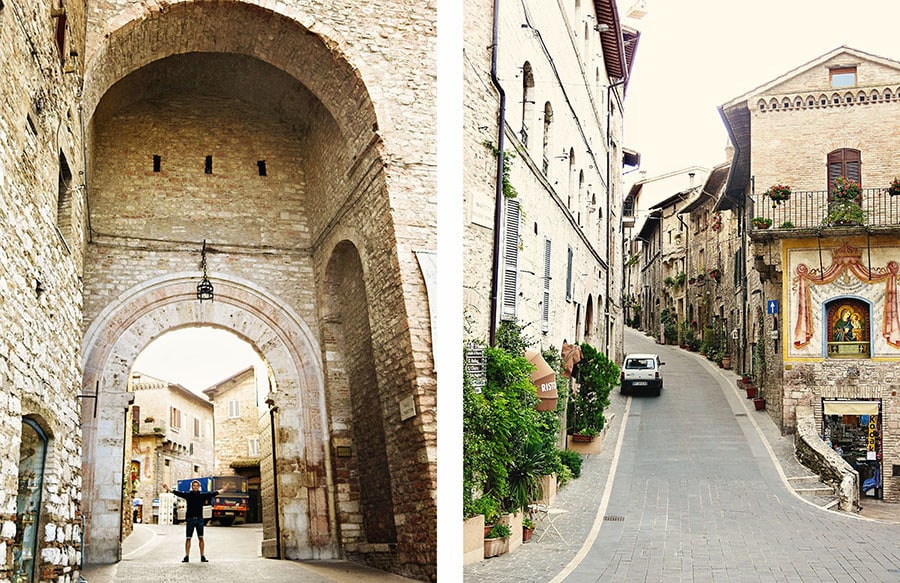 Assisi Italy, man standing in the archway entrance to the old town, narrow street going up between the stone building in old town