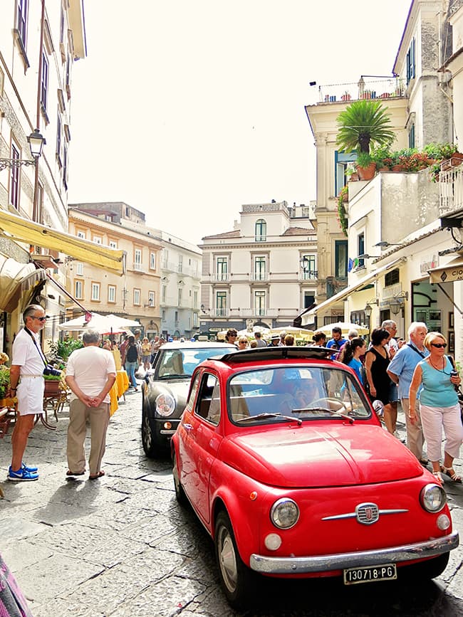 Small red fiat car in the street of Amalfi Town, Amalfi Coast, Italy, tourists on each side of the car