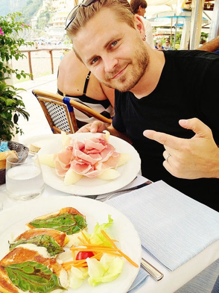 man pointing to a plate of food, Italian cuisine, prosciutto on melon, grilled cheese on leaves, salad