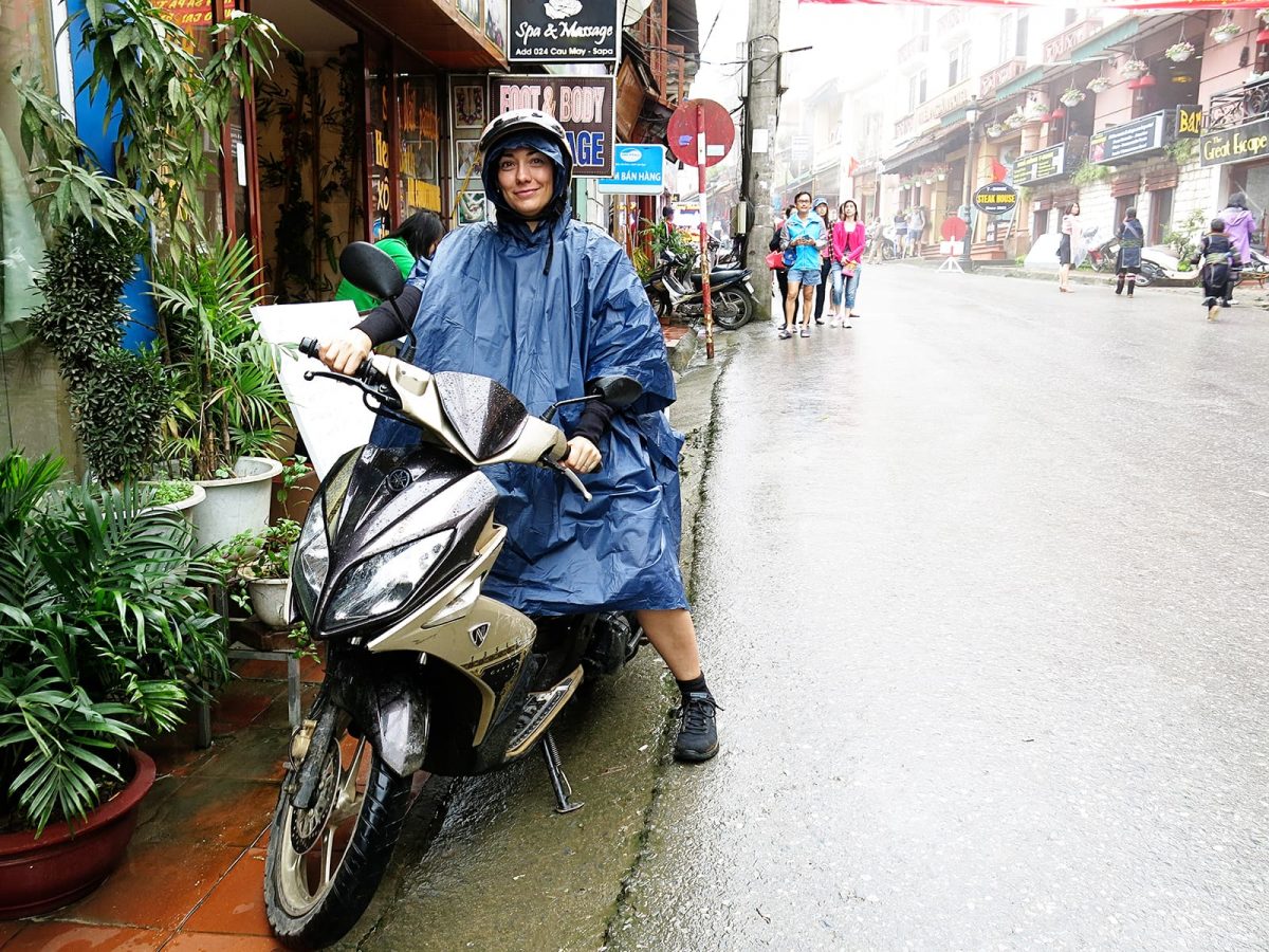 travel-essentials-for-vietnam-poncho, lady in a poncho sitting in the rain on a scooter in a street in Vietman