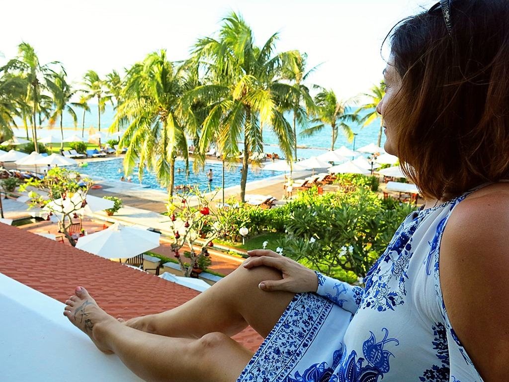 Victoria Hoi An, Vietnam, woman sitting on a ledge, view over the pool area with palm trees