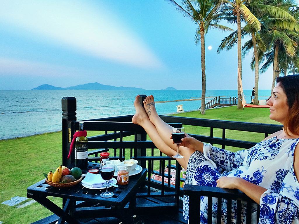 Victoria Hoi An, Vietnam, woman sitting holding a glass of red wine, table with snacks, evening view of the ocean, palm trees and island