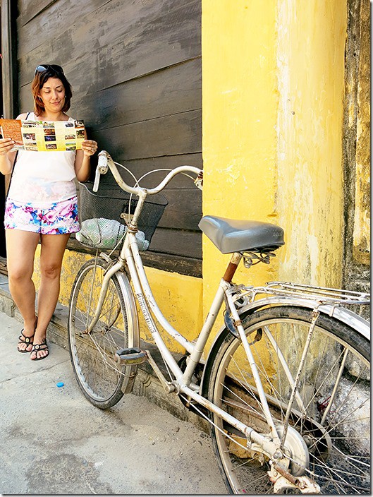 Hoi An Vietnam, woman reading a flyer standing next to a yellow building and bicycle