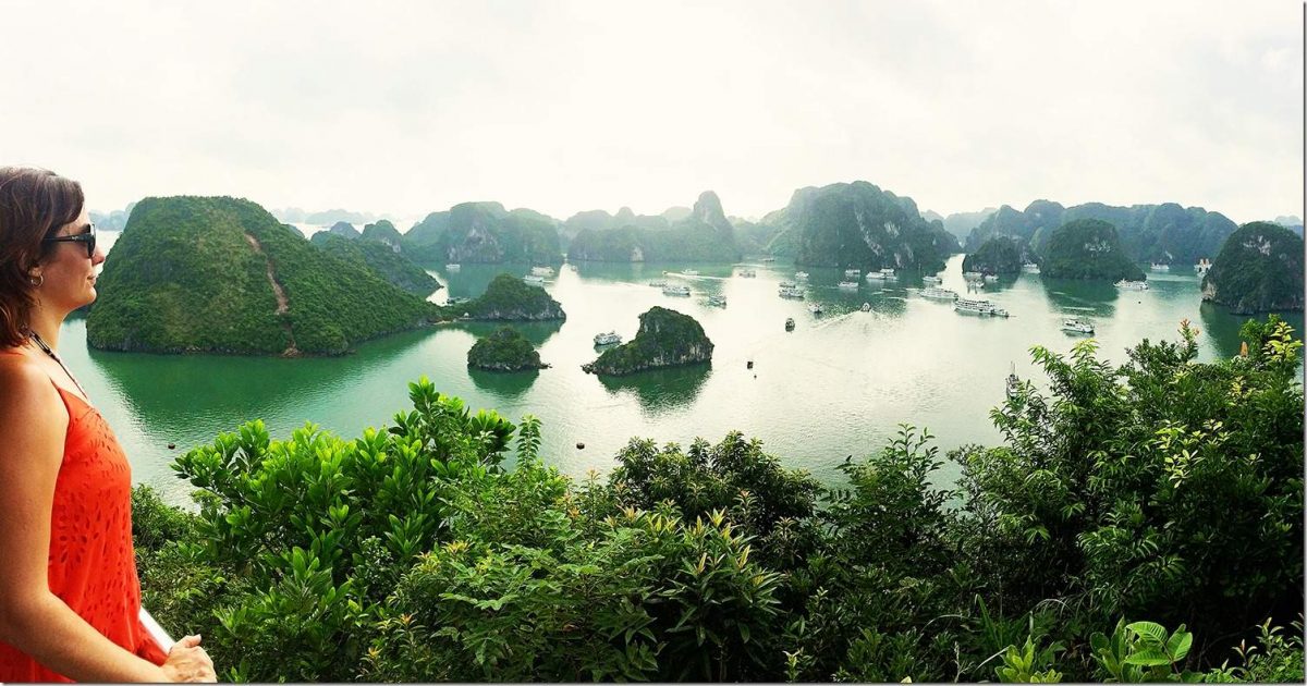 Travel to Vietnam - Ha Long Bay view from the top, woman in orange dress and sunglasses looking out to the bay, boats