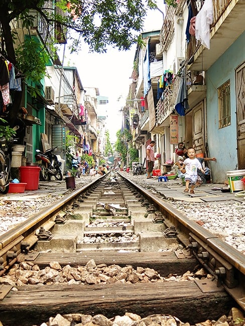 Hanoi train tracks in the city of Hanoi, Vietnam, toddler walking on the side of the track, buildings very close to the tracks