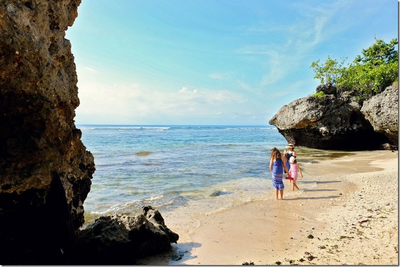 Bali Padang Padang Beach, mother and two daughters walking in the water at the beach, rocks on each side of the small beach