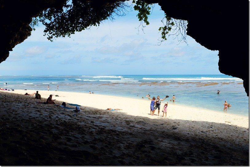 Greenbowl Beach Bali, view from inside the cave onto the beach, family posing for a photo, people sitting in the shade and some swimming