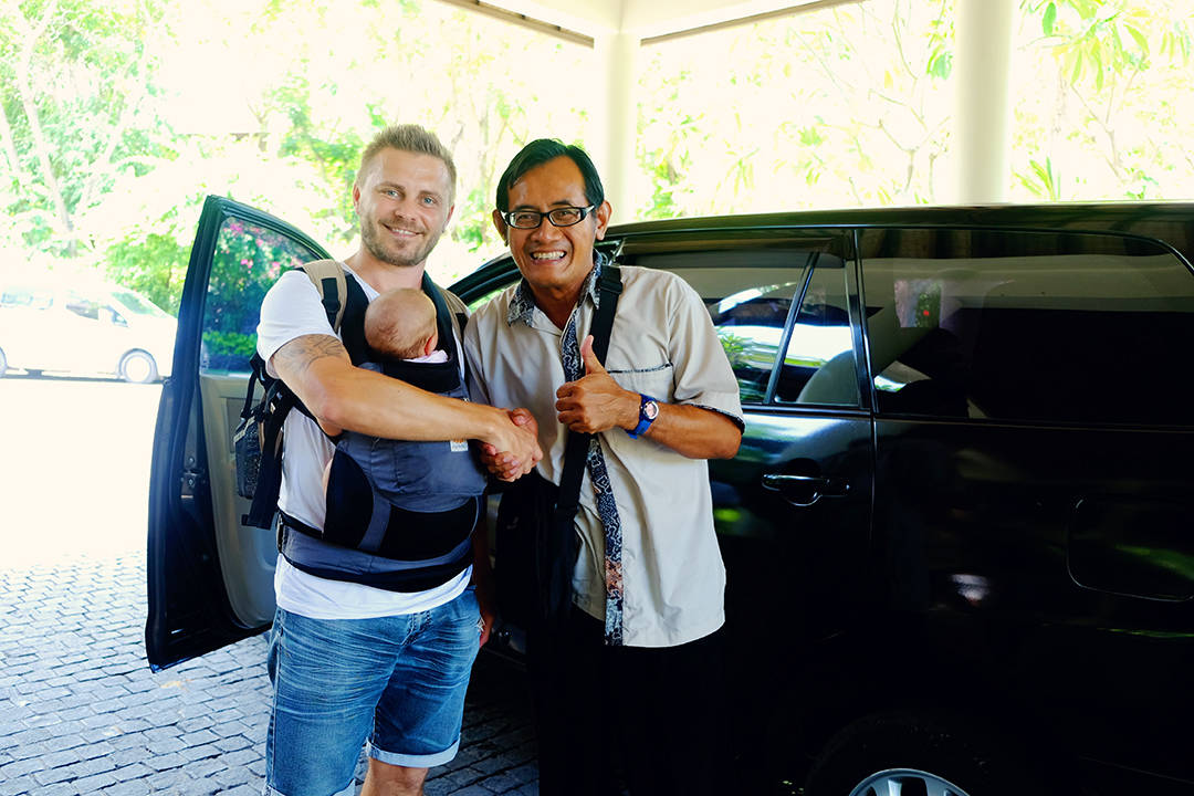 Stories about Local Way of Bali Life, man shaking hands with a driver in Bali, man with a baby in the baby carrier