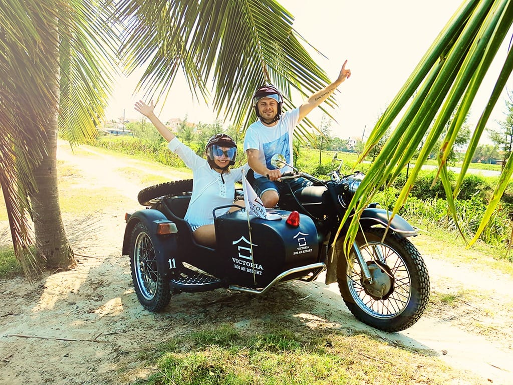 Travelling on a Motorcycles - Hoi An Vietnam, Victoria Hoi An, Vietnam side cart motorcycle, man and woman arms up, rural road, palm trees