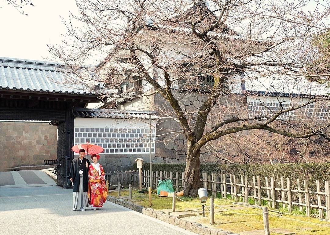 Kanazawa Castle Park, Japan, a couple dressed in traditional Japanese clothing, man in clack and holding a red umbrella, lady in red kimono