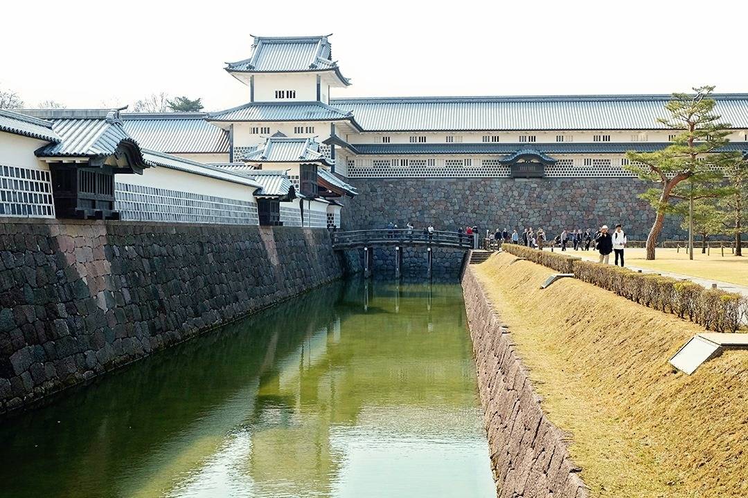 View of the castle from the outside, some tourist walking around, fortified walls and water pit around the castle