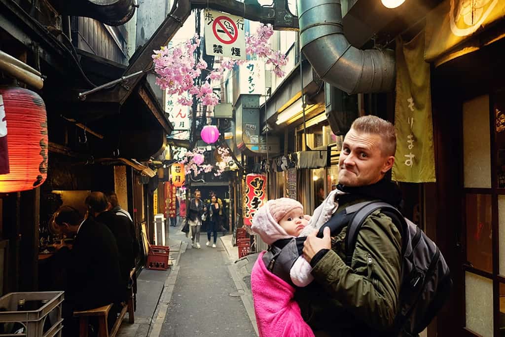 Piss Alley Tokyo Japan, father holding a baby in the baby carrier, standing in a small alley