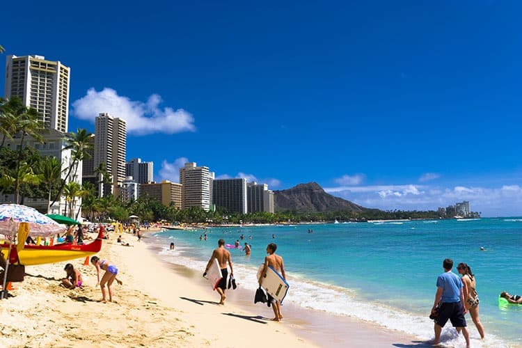 Hawaii, USA, beach view, people walking with boards, kids playing, blue water, hotels on the shoreline, mountain in the distance