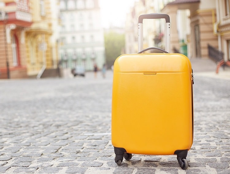 Orange suitcase on the road in city. Summer vacation and travel concept