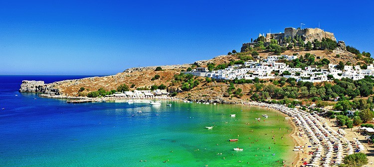 scenic Rhodes island, Lindos bay. Greece, view of the beach, beach umbrellas and white buildings of the town in the far