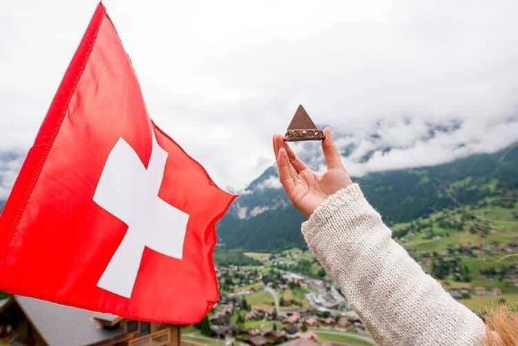 Holding traditional chocolate in form of triangle with swiss flag on the mountain background in Switzerland