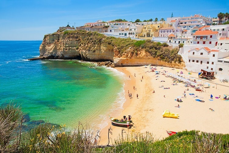 The Algarve in Portugal, view from above over the beach, people at the beach, beach umbrellas, town buildings, rocky coastline