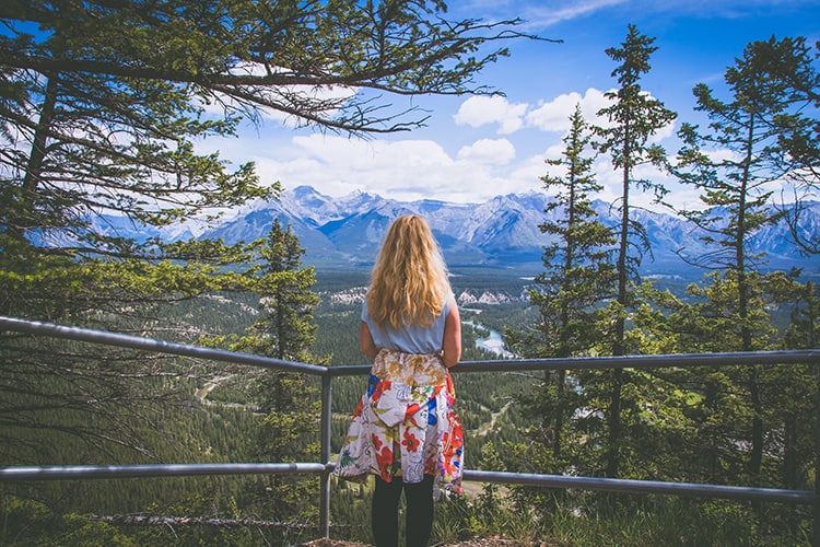 Banff National Park Canada, woman looking away towards the mountains from the view point, tall trees 
