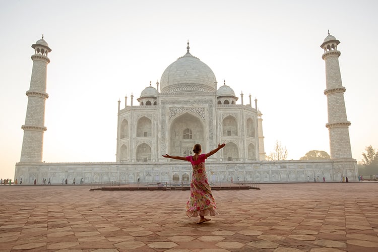 Woman standing in the red dress arms up in front of the Taj Mahal