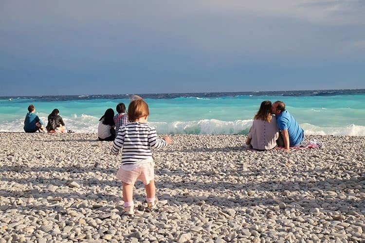 Stone beach in Nice, France, toddler walking on the stones, couples sitting and kissing