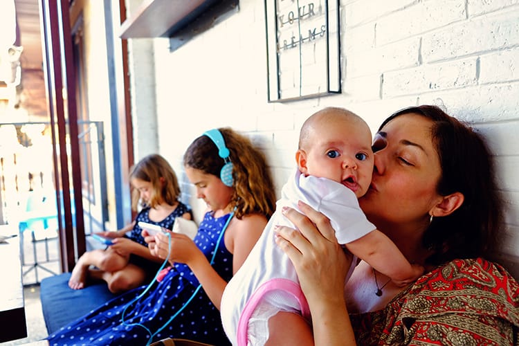 Bali, Indonesia, Mother holding and kissing a baby, baby looking into the camera, two young girls on technology, playing games