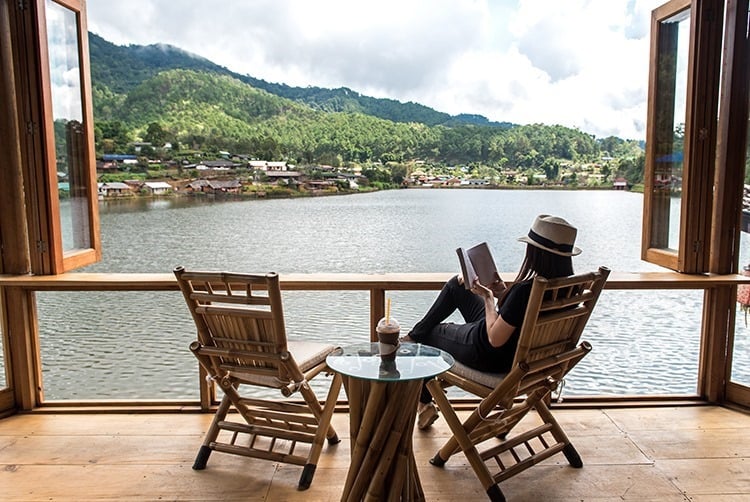 Lady reading a book, sitting in a chair with a water view