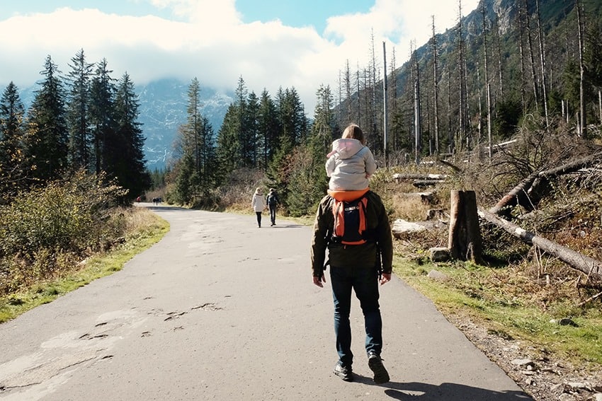 Zakopane in Poland with Kids, father with toddler sitting on his shoulders walking on the road, forest and mountains