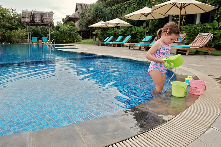 Telunas Private Island, Indonesia, toddler playing in the pool with beach toys, sun loungers and umbrellas in the background