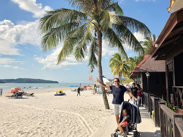 Langkawi in Malaysia, man standing close to the beach with a toddler in the pram, beach and palm trees