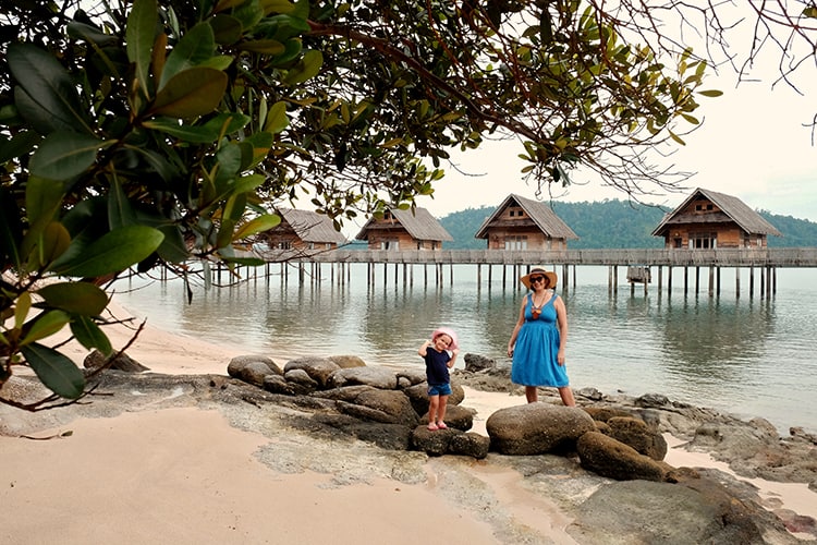 Telunas Private Island, Indonesia, mother and a toddler standing on the rocky beach with over water villas in background