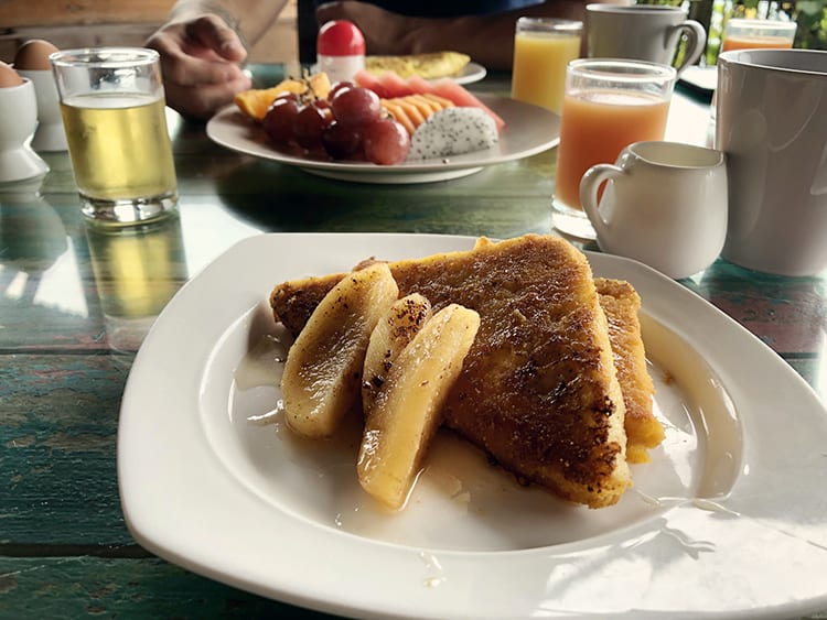 breakfast tropical fruit chopped up, juices, tea cups, French toast with roasted pears on the white plate