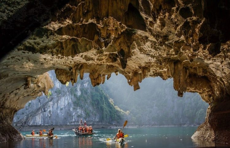 Bat cave in Halong Bay Vietnam, people on a boat and kayaks going in though a cave in the water