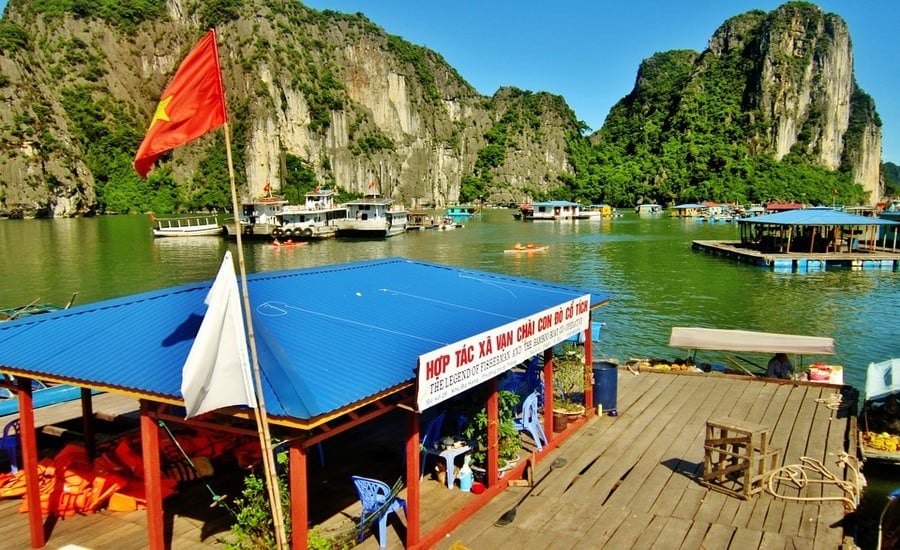 Halong Bay floating village in Vietnam, floating platform with blue roof, red flaf, boats and rocky islands in background