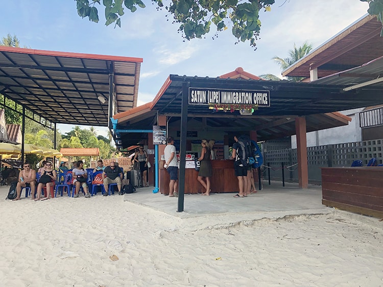 Immigration Office on Koh Lipe Thailand, Satun, people standing at the office, people sitting on plastic chairs in the sand