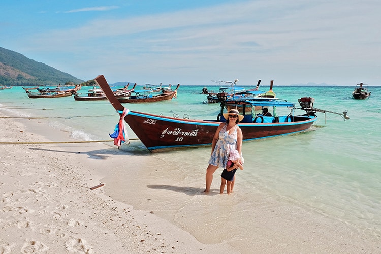 Sunrise Beach Koh Lipe Thailand, mother and daughter standing in the water at the beach, long tail boats parked