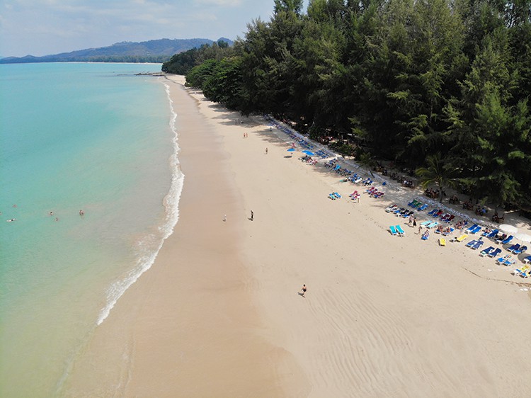 Aerial view of a large sandy beach, some people swimming, walking and beach sun loungers