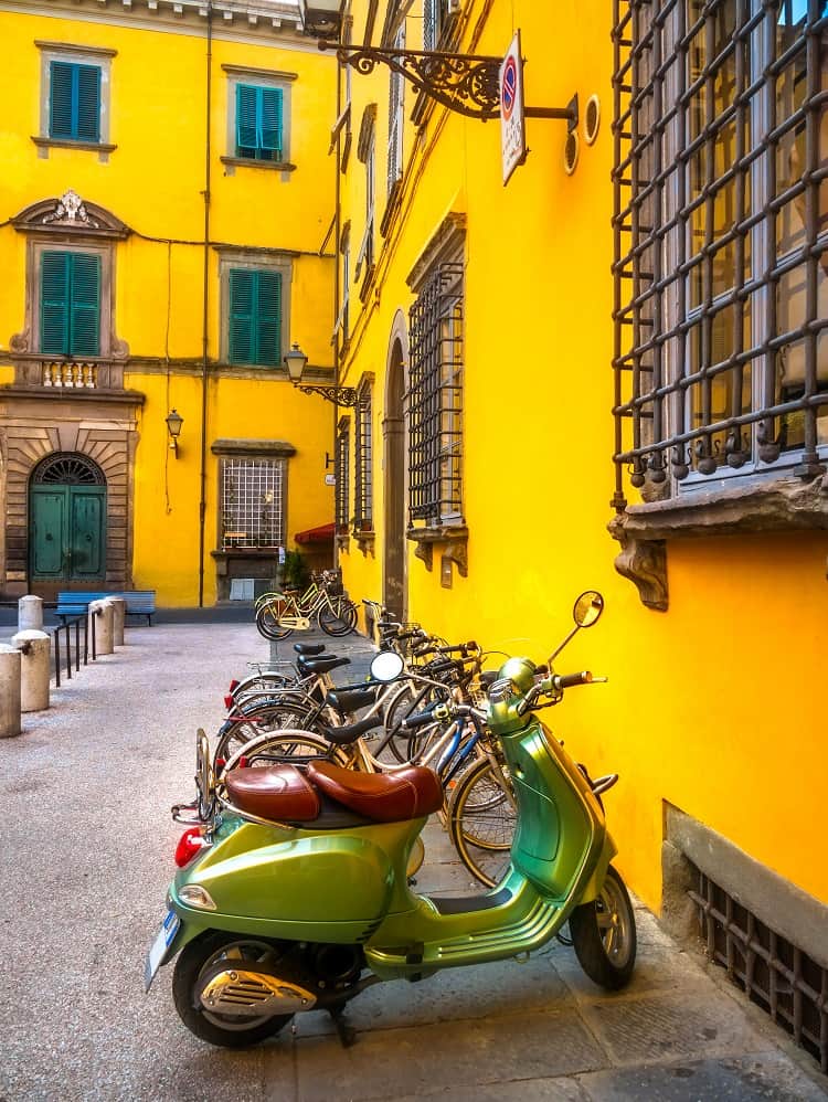 Lucca Italy, green scooter and bicycles parked next to a bright yellow building