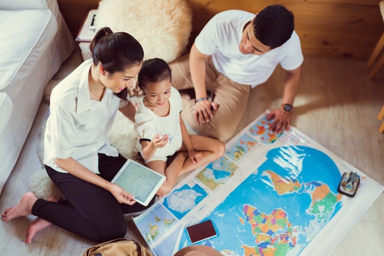 Planning for your next family vacation, family sitting on the floor and looking at a world map, ipad