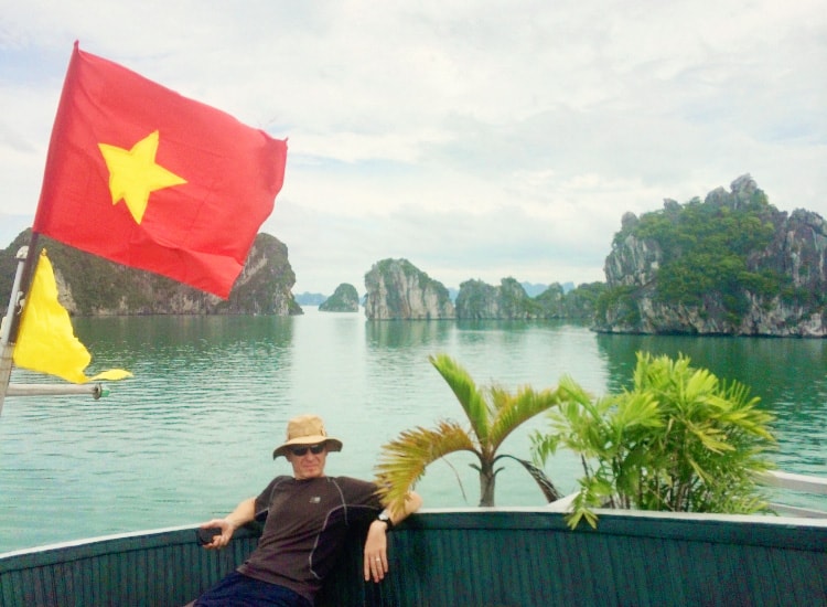 Halong Bay Cruise, Vietnam, man sittin on the top deck of the junk boat, water and rocky island in the back