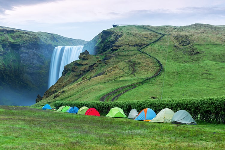 Iceland Camping, tents along the side of the bushes, green grassy hills and mountains, big waterfall 