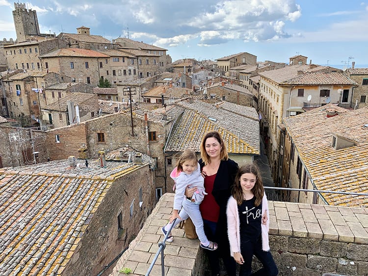 tuscan villages to visit - Volterra, Italy, mother and two daughters posing on a roof top, roof tops of the old town in bcakground