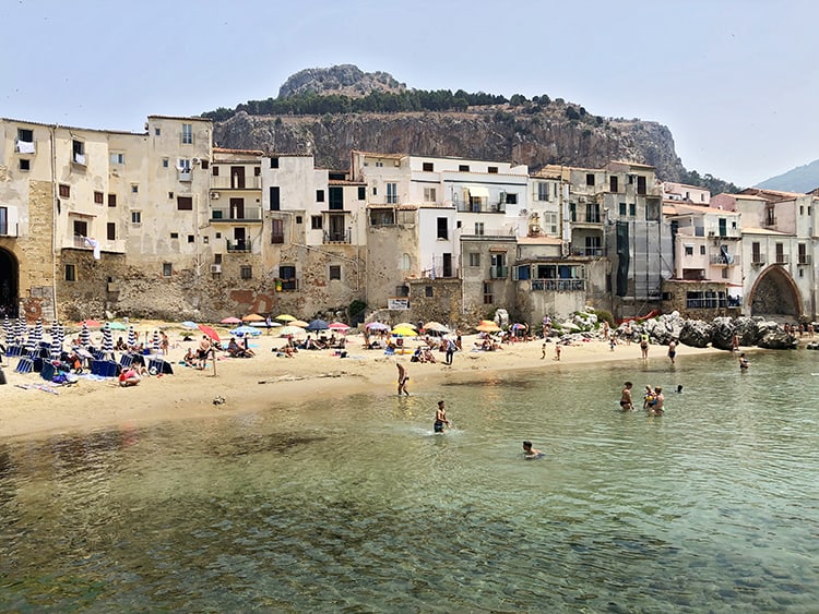 Cefalu Italy, view of the beach side town, people swimming, people on the beach, beach umbrellas, buildings, mountain in the back