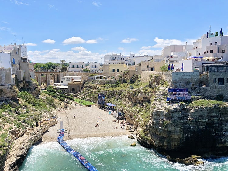 Polignano a Mare Puglia Italy, view of the beach, buildings at the tops of the cliffs, floating pier from the beach into the water