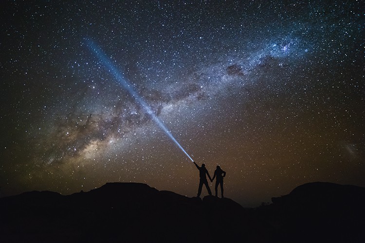 a couple at night shinning light from a flash light into the dark starry sky