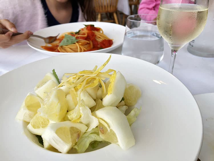 Lemon Salad Procida served on a white plate, white wine glass and spaghetti with tomato sauce