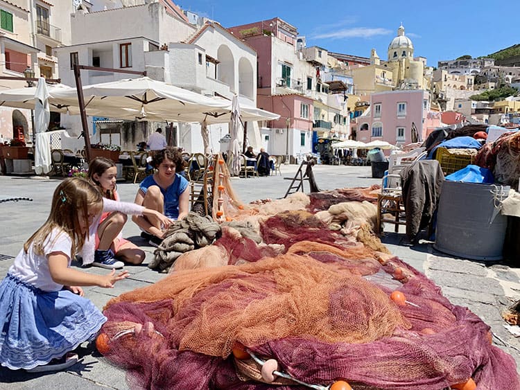 Procida in Italy, there young girls playing with the fishing net in Marina Corricelli, red and orange colour net 