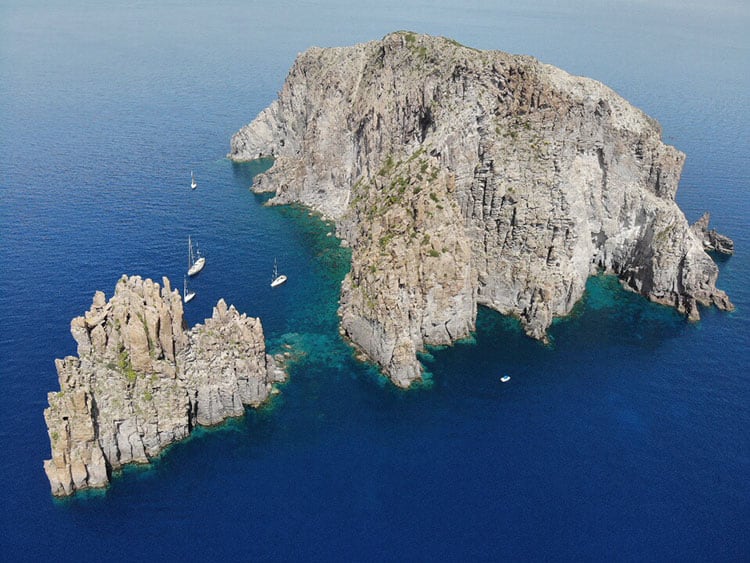Boating Around Panarea Island Sicily, Italy, drone view of the rocky island, small white sailing and motor boats below