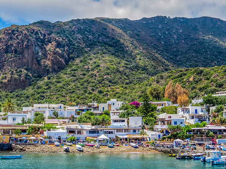 View of the island of Panarea, Aeolian Islands, Italy, white buildings, rocky beach, mountains in the background