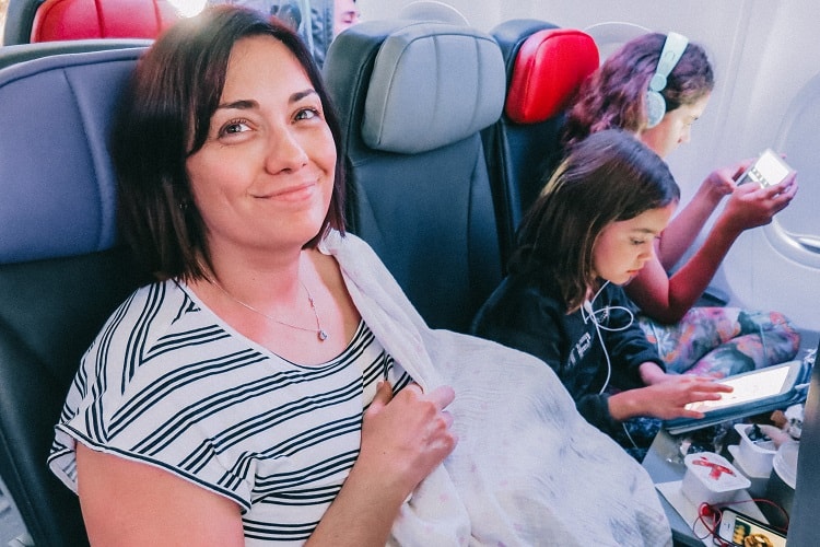 Mother and two daughters sitting in the airplane seats, mother holding a baby covered by a cloth, smiling